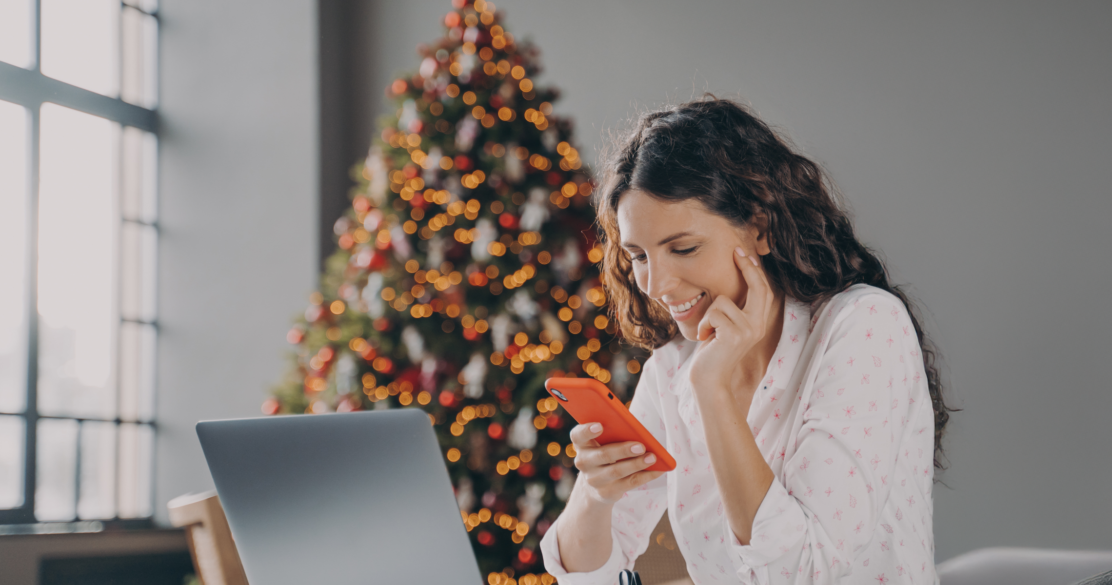 Mujer sentada con telefono en mano y detras hay un arbol de navidad