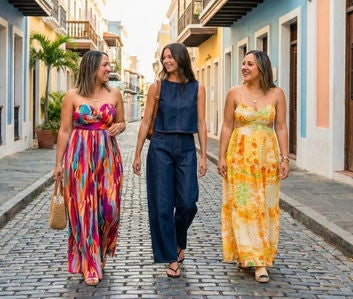 Tres mujeres caminando por calle adoquinada con vestidos coloridos y azul.