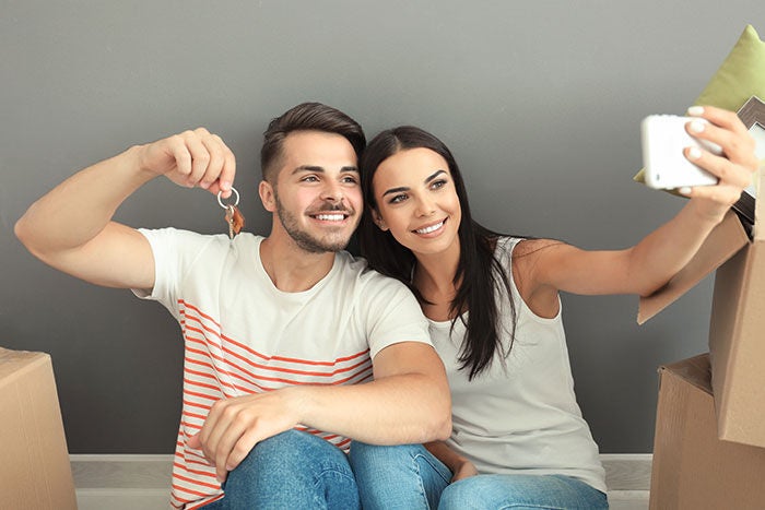 Young happy couple taking selfie with house key at new home