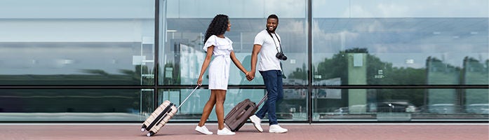 couple holding hands while dragging suitcases