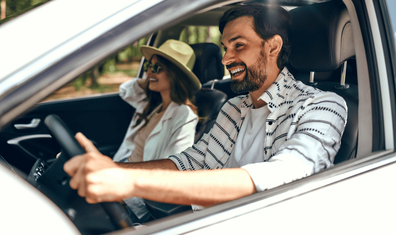 Hombre conduciendo su auto mientras sonríe con su pareja como copiloto. 