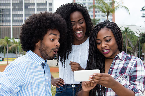 Three friends laughing while watching something on a cell phone.