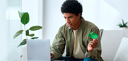 Young man on his laptop and with a card in his hand