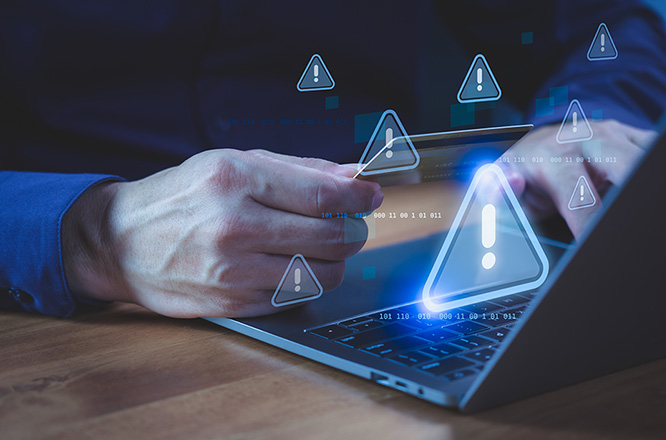 Person holding a credit card while using a laptop computer with warning symbol, representing online payment risk, online shopping, financial fraud, and identity theft during digital transactions.