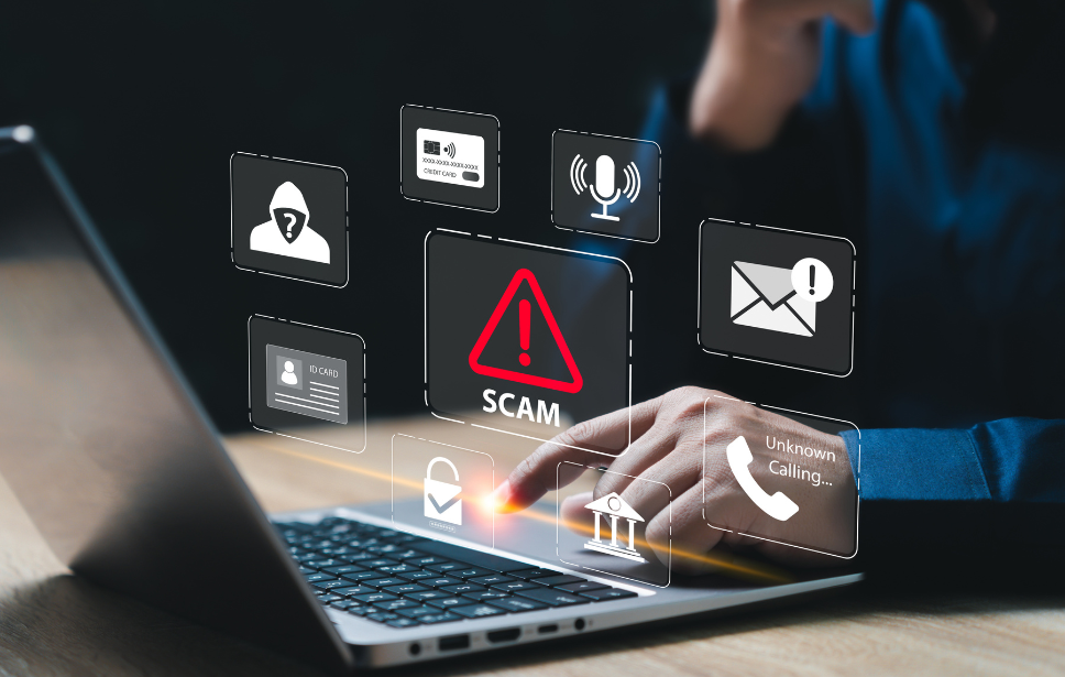 Mano utilizando una laptop mientras aparecen íconos digitales relacionados con estafas, seguridad y alertas de fraude, incluyendo un símbolo de advertencia con la palabra “SCAM”.