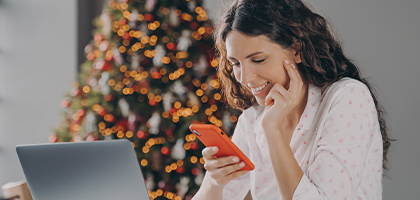 Mujer sentada con telefono en mano y detras hay un arbol de navidad